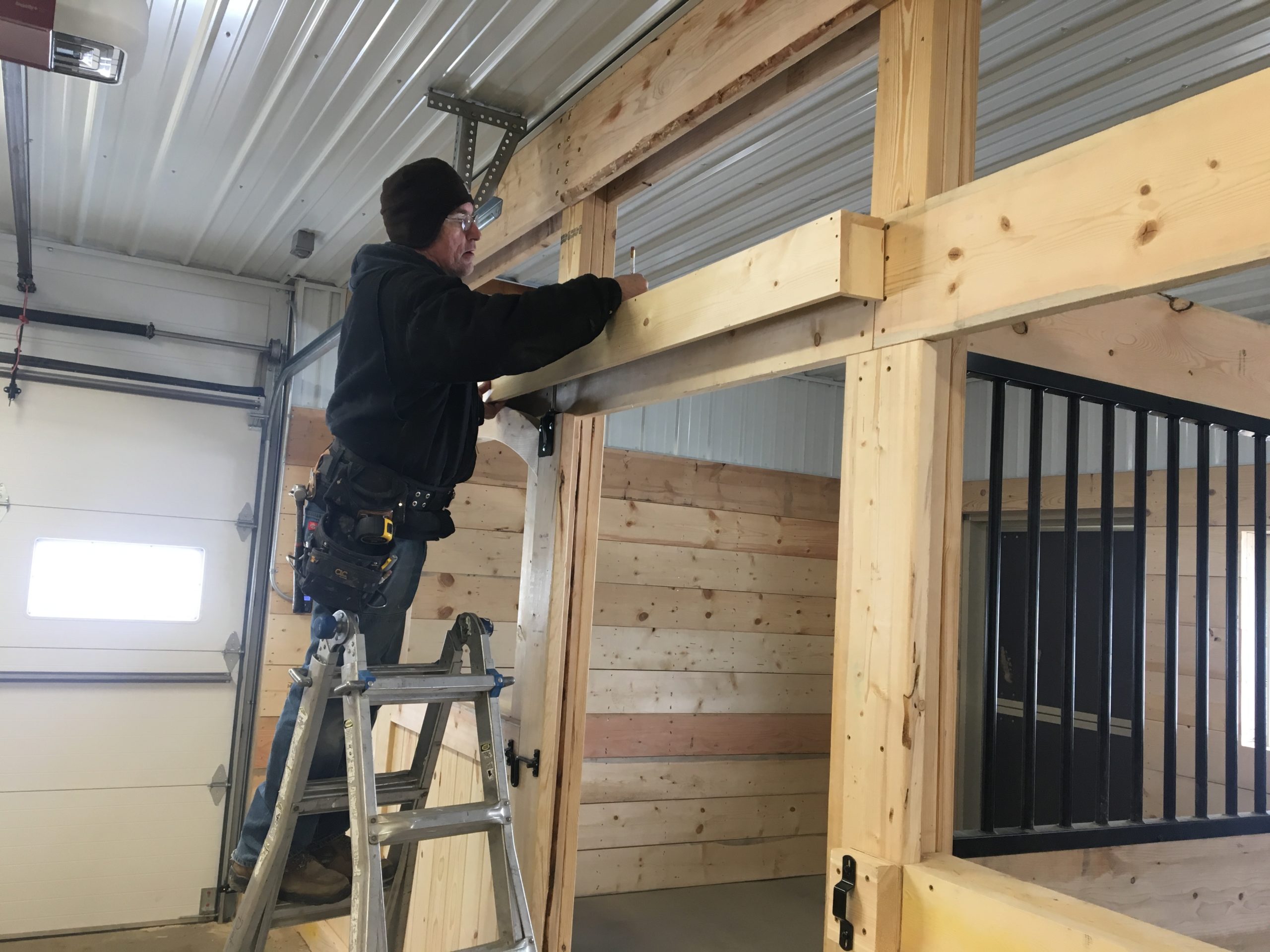 Independent contractor stands on a ladder to work on a construction project measuring and making wood